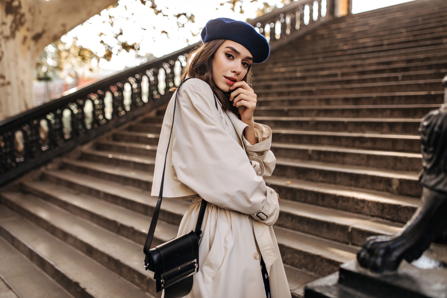 lovely-young-parisian-woman-with-brunette-hair-stylish-beret-beige-trench-coat-black-bag-standing-old-stairs-sensitively-posing-outdoors